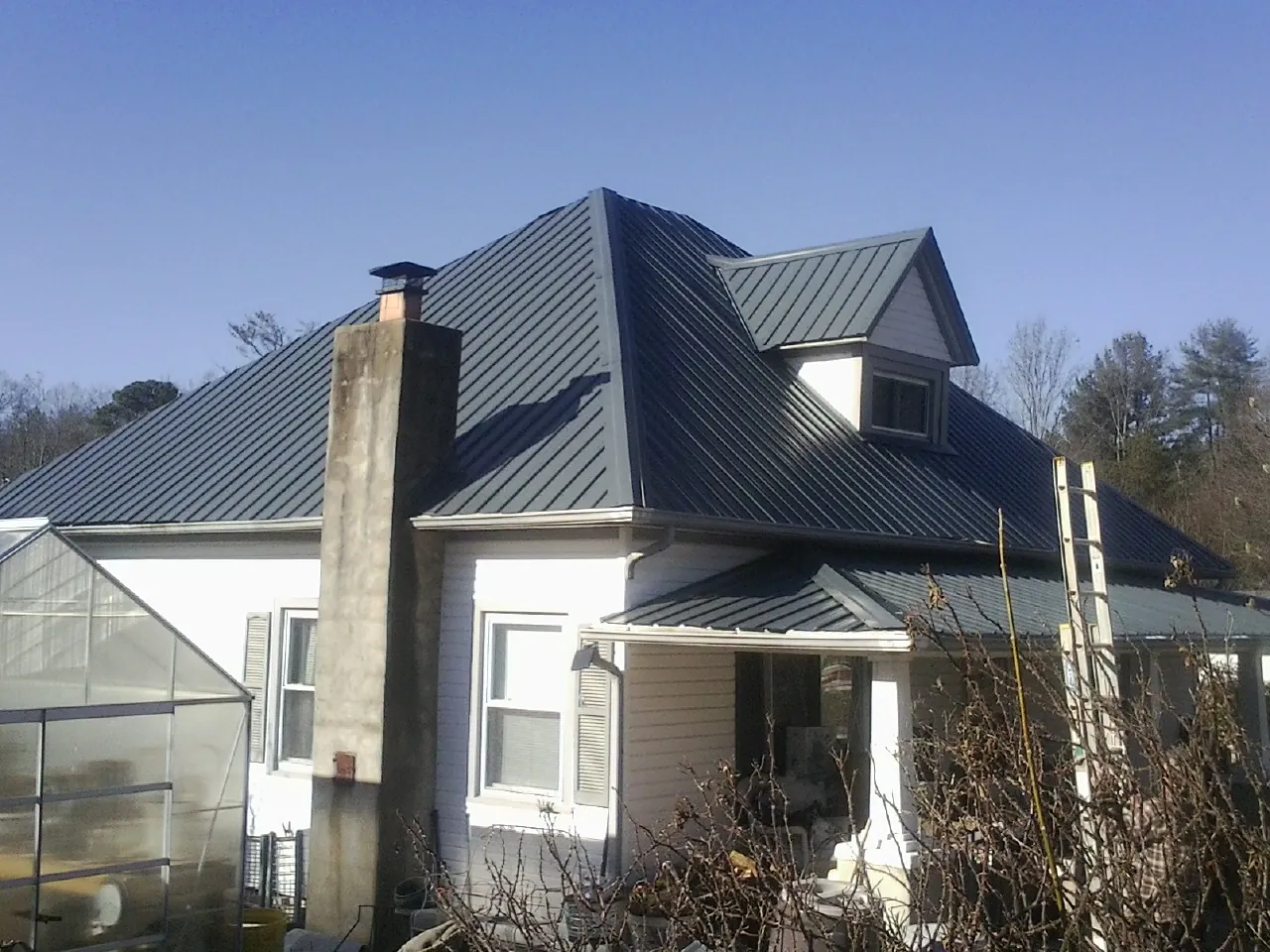 Dark blue standing seam metal roof on a white farmhouse with dormer — Slate & Tile Roof Repair by Roofing Brothers in Postville