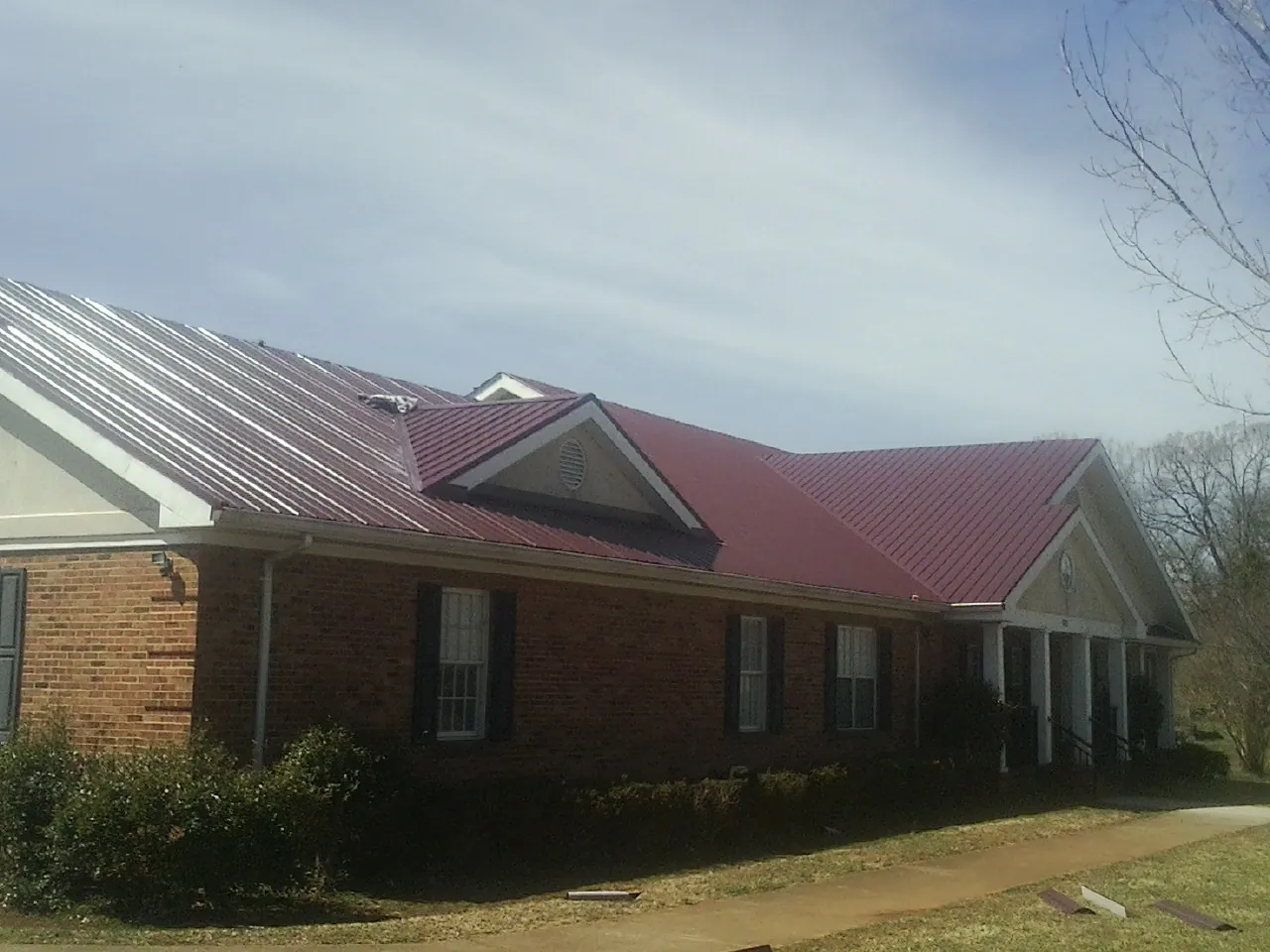 Red metal roof with gabled entries on a long brick building, from a Hail Damage Roof Repair job in Postville