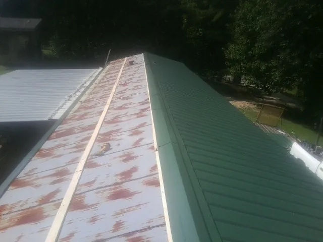 Old rusted panels beside newly installed green metal roofing — Wind Damage Roof Repair by Roofing Brothers in Postville