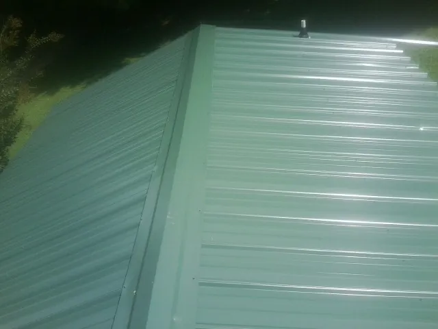 New green metal panels meeting at the ridge of a roof — Flat Roof Repair work by our crew in Postville