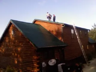 Crew on the ridge of a green metal roof on a two story log home in Postville