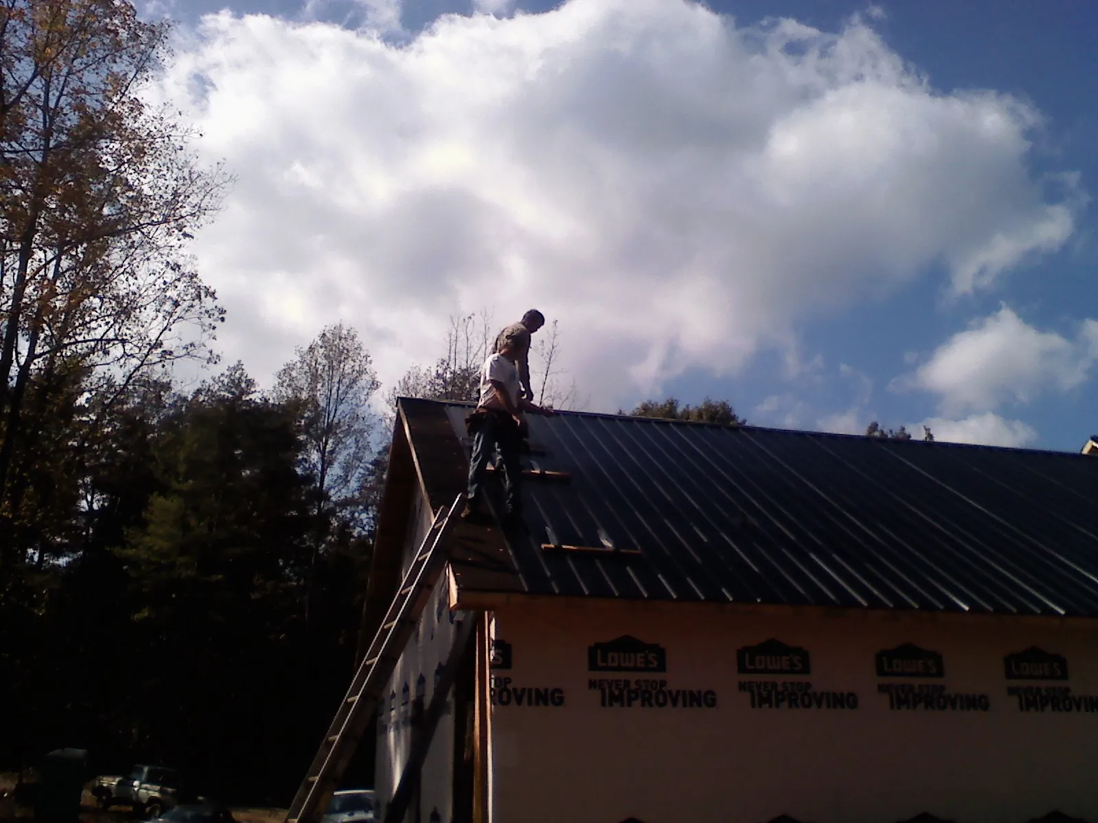 Roofer fastening dark metal panels high against a cloudy sky, from a Roof Inspection job in Postville