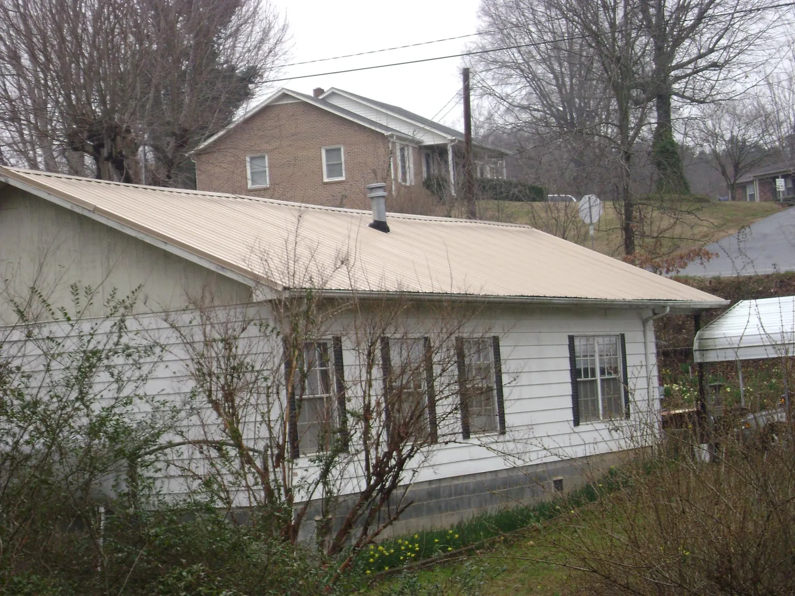 Tan metal roof on a white sided house set into a hillside — Commercial Roofing by Roofing Brothers in Postville