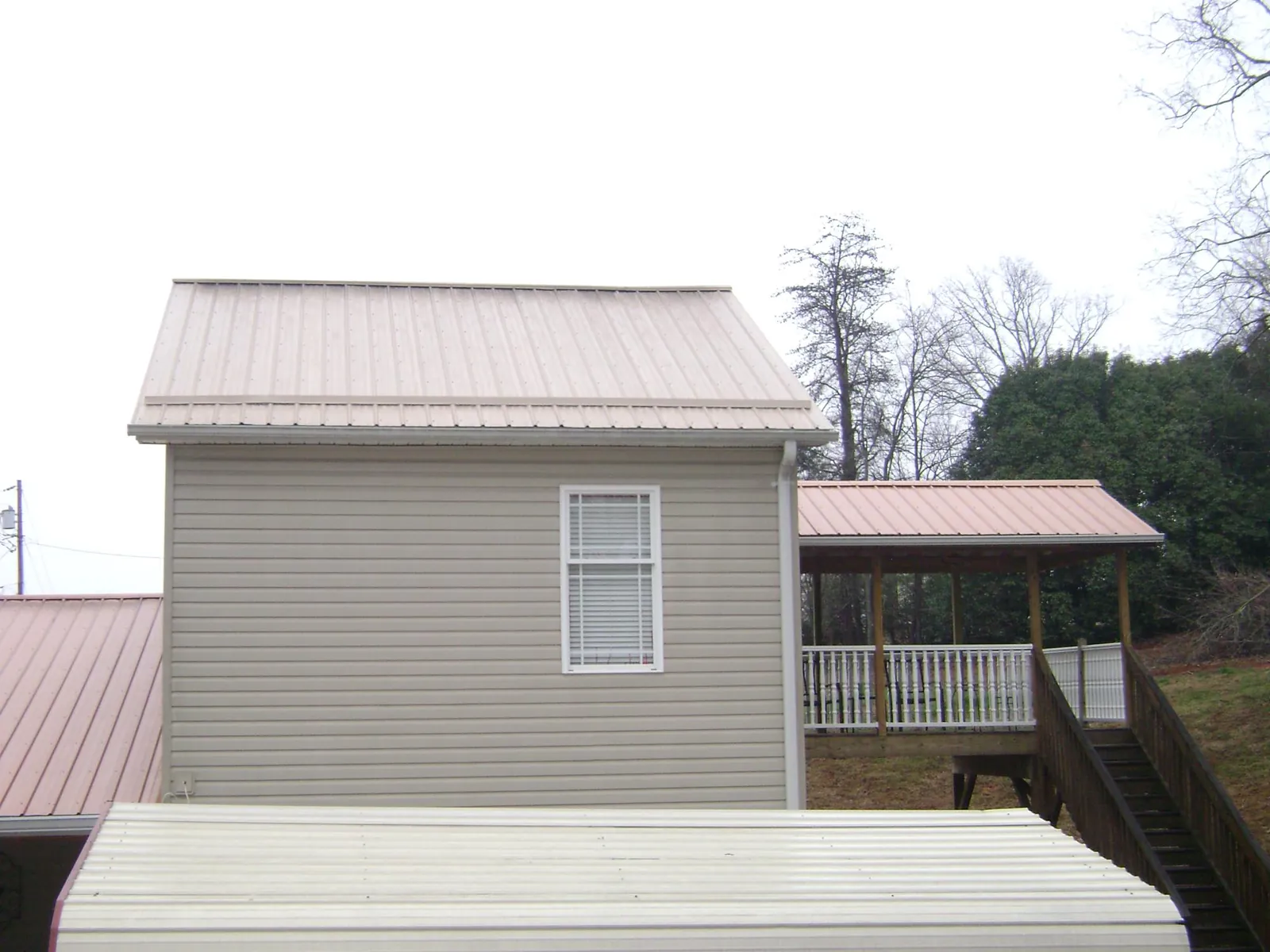 Tan metal roofs on a two story addition and attached porch, from a Roof Replacement job in Postville